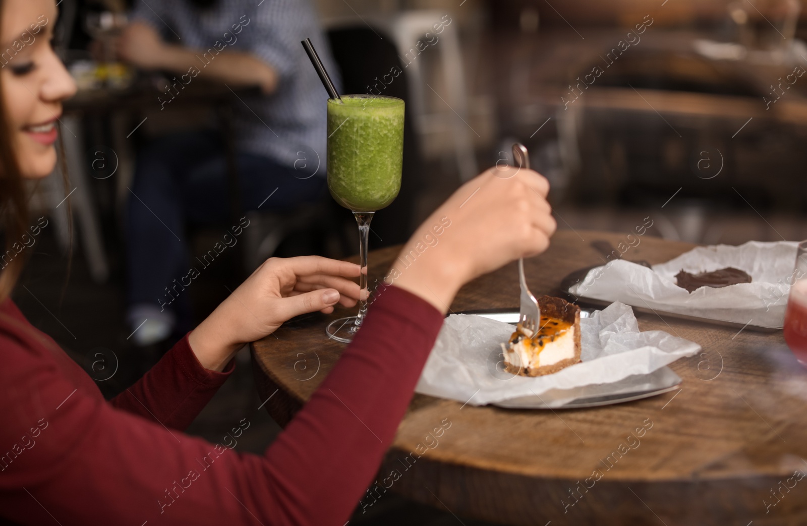 Photo of Pretty young woman with cocktail and cake at table in cafe, view from outdoors through window