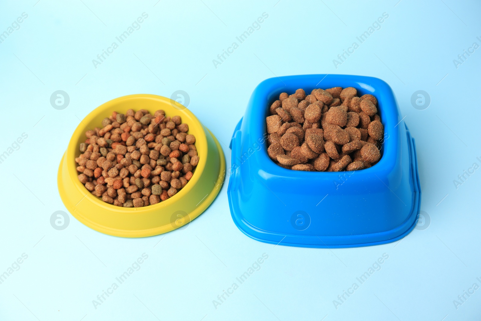 Photo of Dry pet food in feeding bowls on light blue background