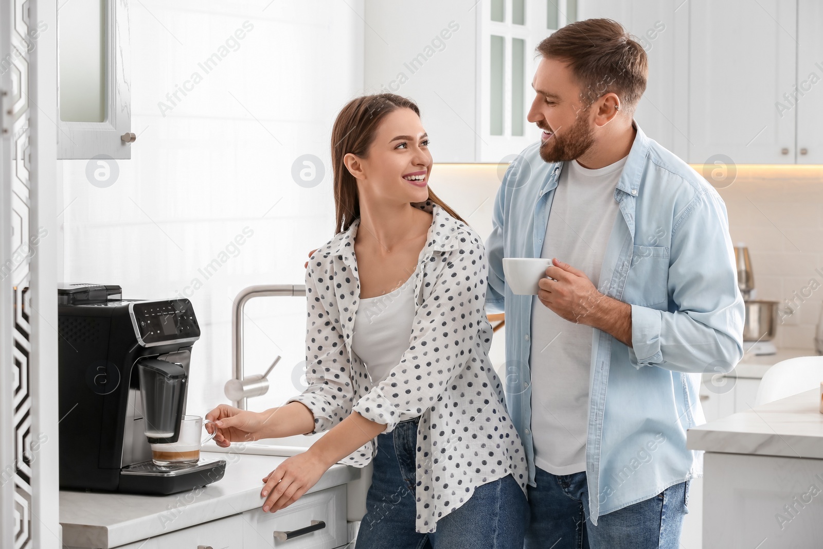 Photo of Happy couple preparing fresh aromatic coffee with modern machine in kitchen