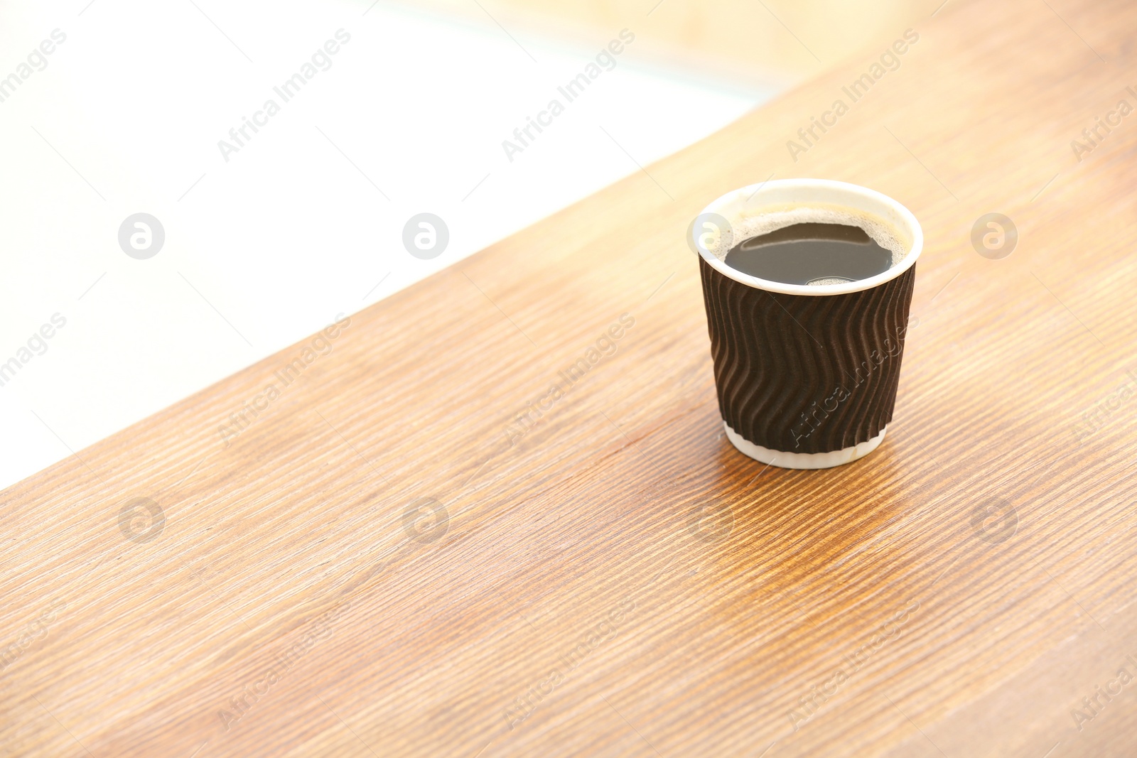 Photo of Cardboard cup of coffee on wooden table. Space for text