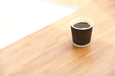 Cardboard cup of coffee on wooden table. Space for text