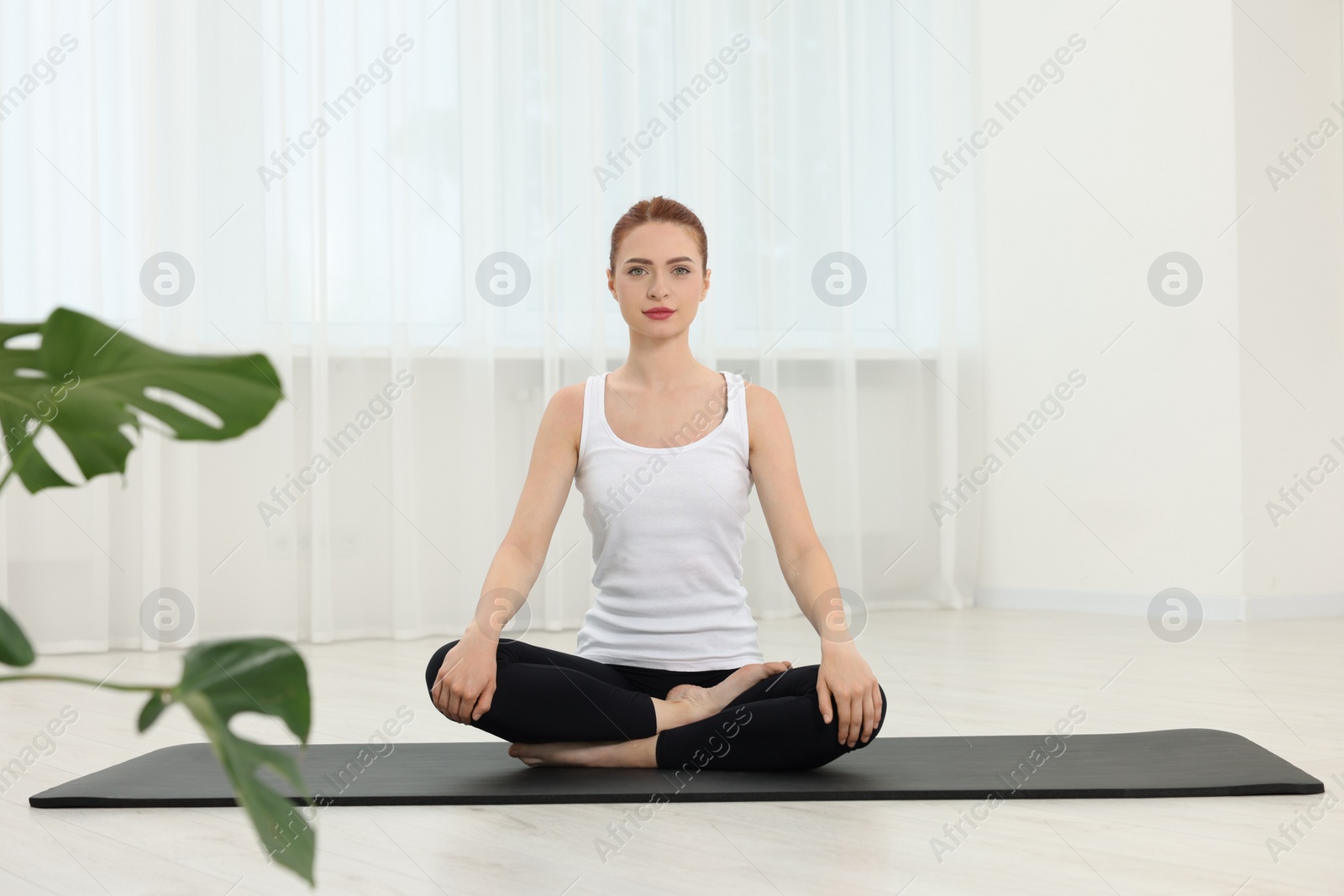 Photo of Young woman practicing yoga on mat indoors