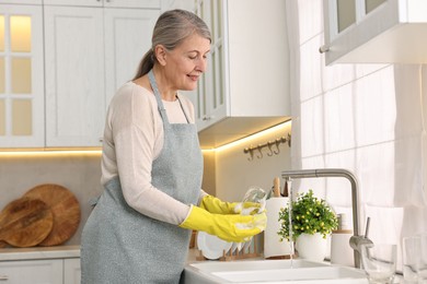 Happy housewife washing glass in kitchen sink