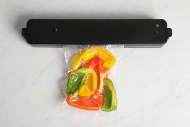 Photo of Sealer for vacuum packing with plastic bag of bell peppers on white table, flat lay