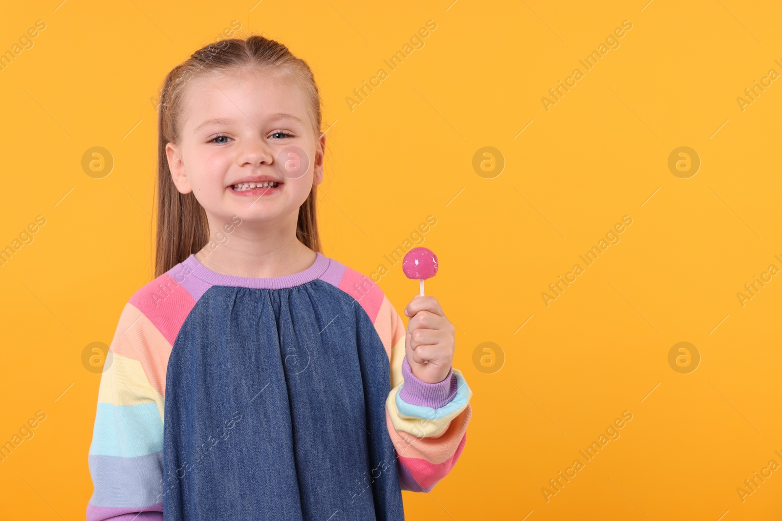 Photo of Happy little girl with lollipop on orange background, space for text