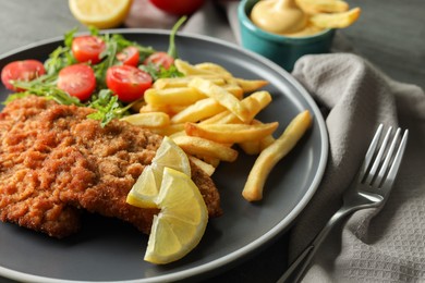 Tasty schnitzels served with potato fries, tomatoes and arugula on grey table, closeup