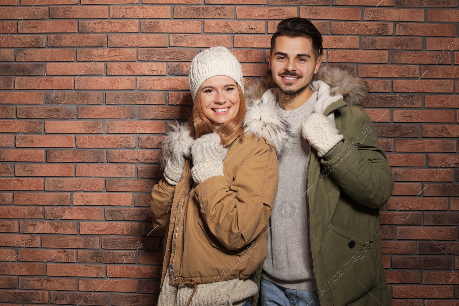 Photo of Young couple wearing warm clothes against brick wall, space for text. Ready for winter vacation