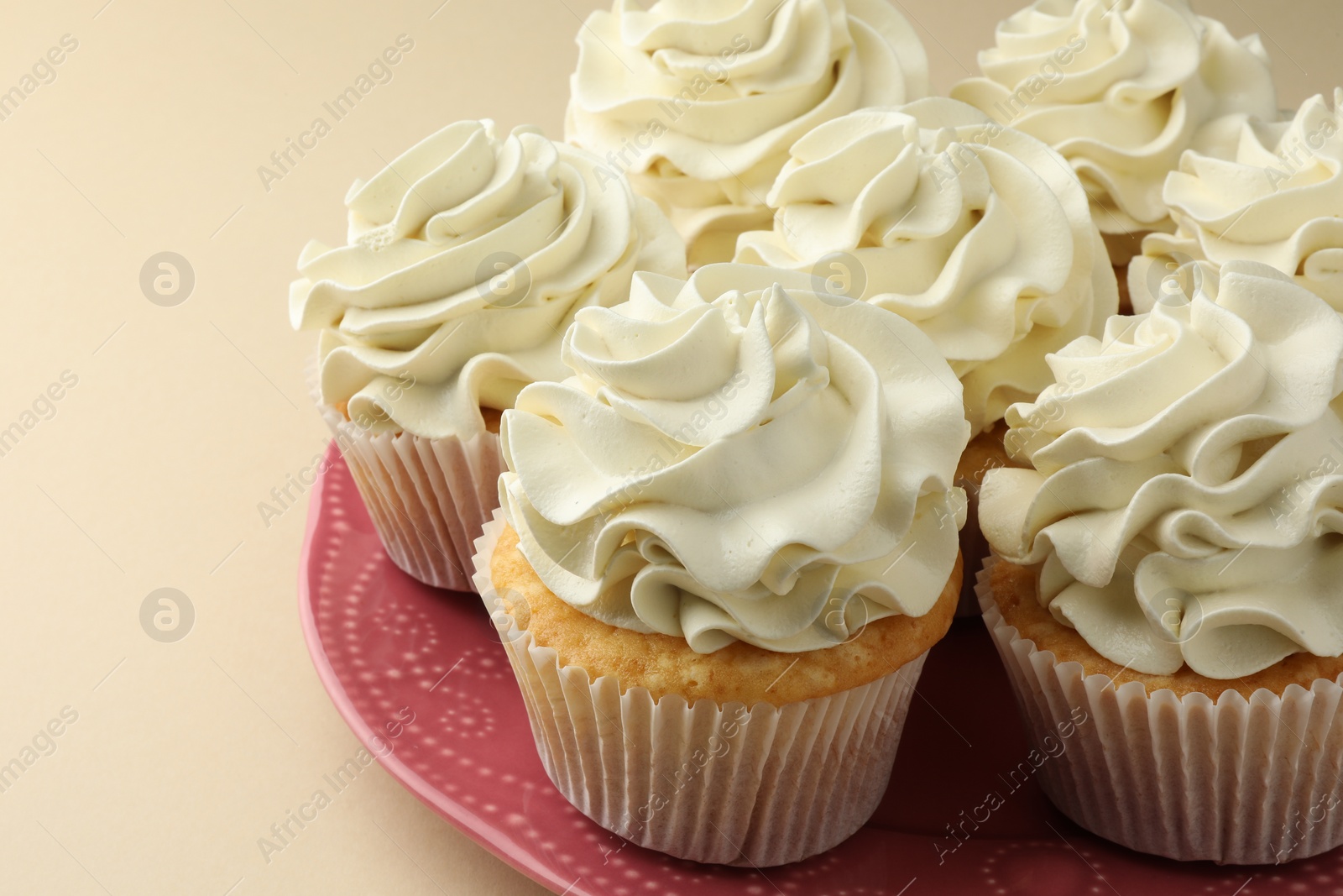 Photo of Tasty vanilla cupcakes with cream on beige table, closeup