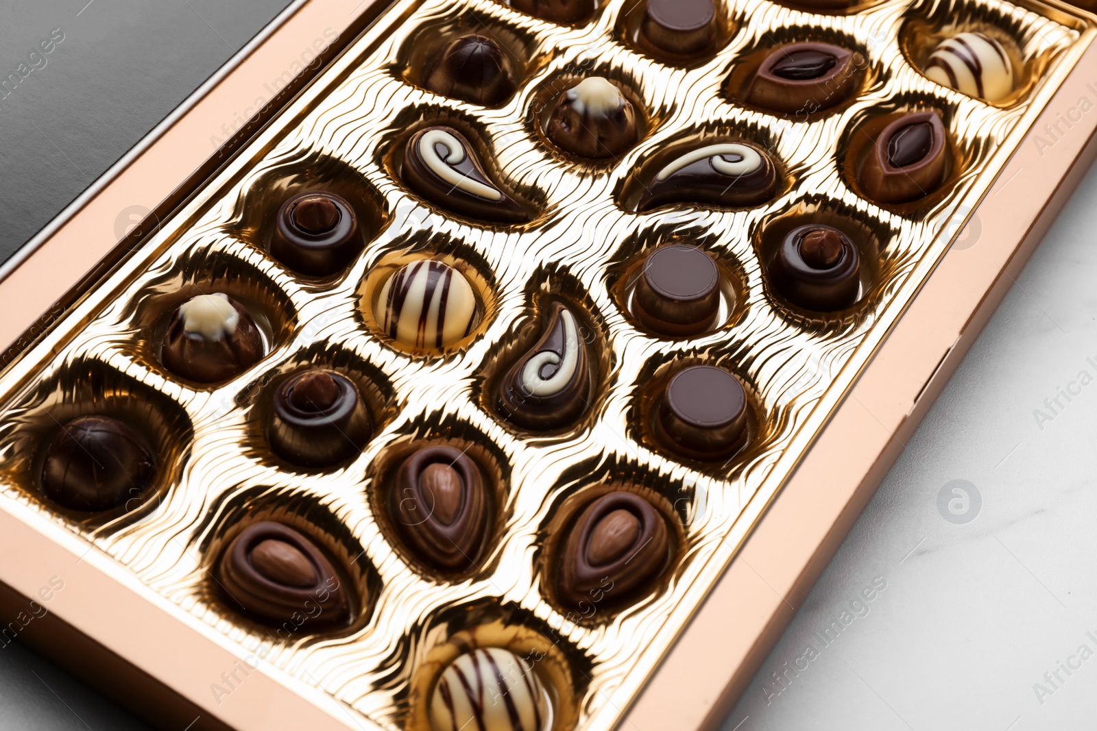 Photo of Box of delicious chocolate candies on white marble table, closeup