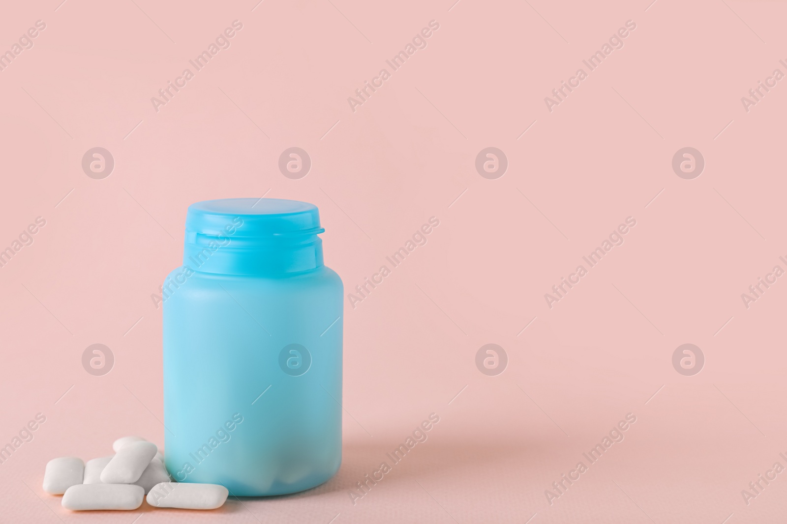 Photo of Jar with chewing gums on light pink background. Space for text