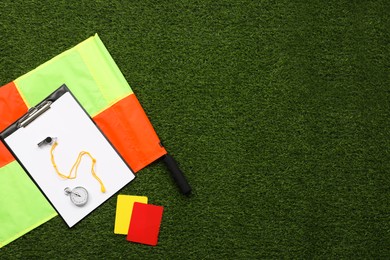 Photo of Different referee equipment on green grass, flat lay. Space for text