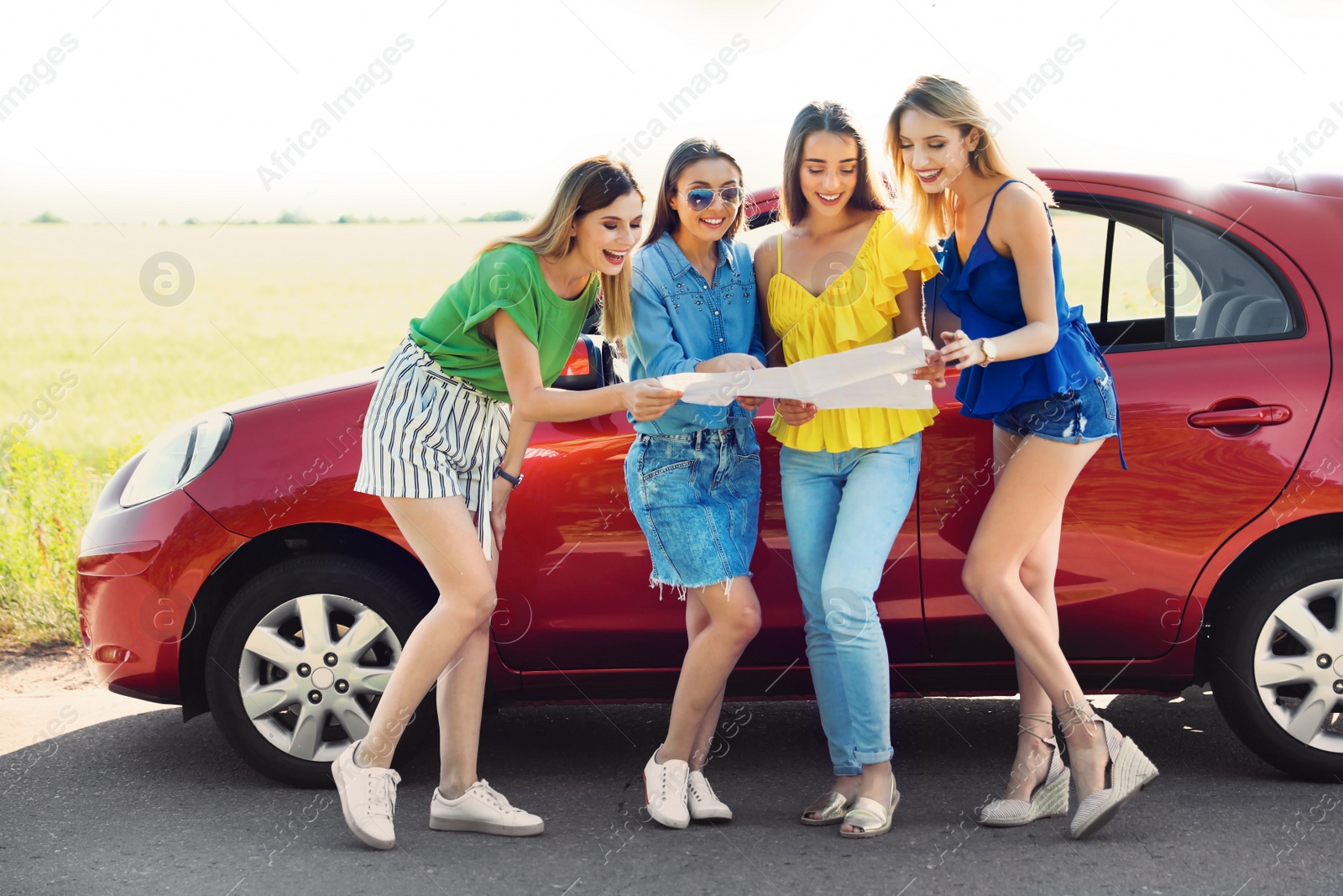 Photo of Happy beautiful young women with map standing near car in countryside