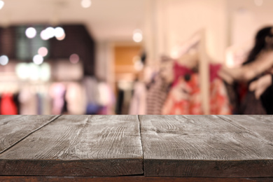 Empty wooden table and blurred view of store with modern clothes