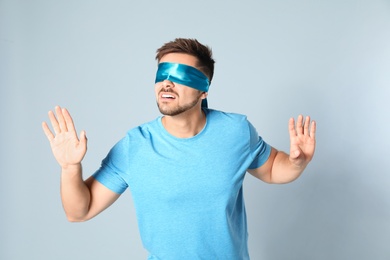 Young man with light blue blindfold on grey background