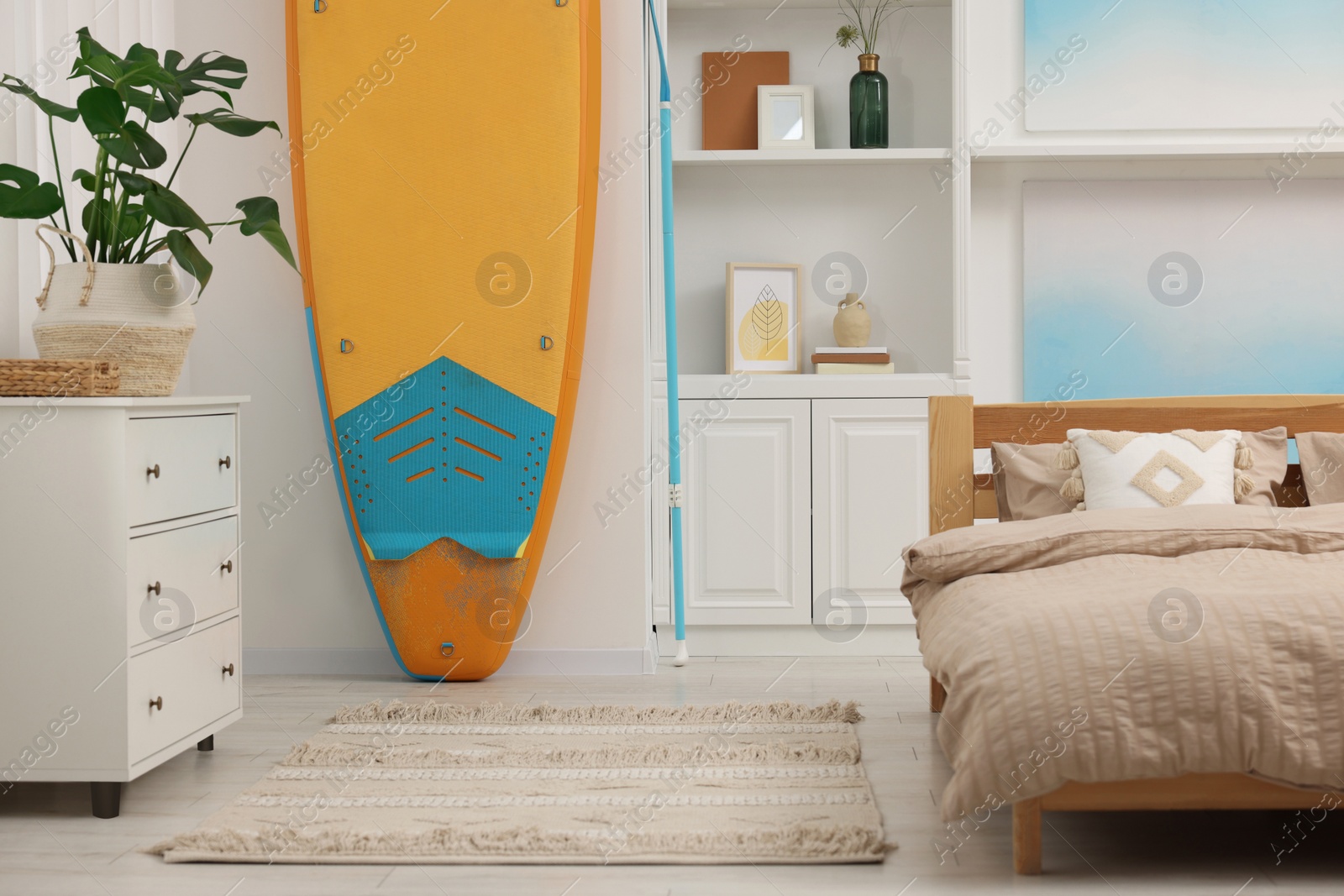 Photo of SUP board, bed and furniture in room. Interior design