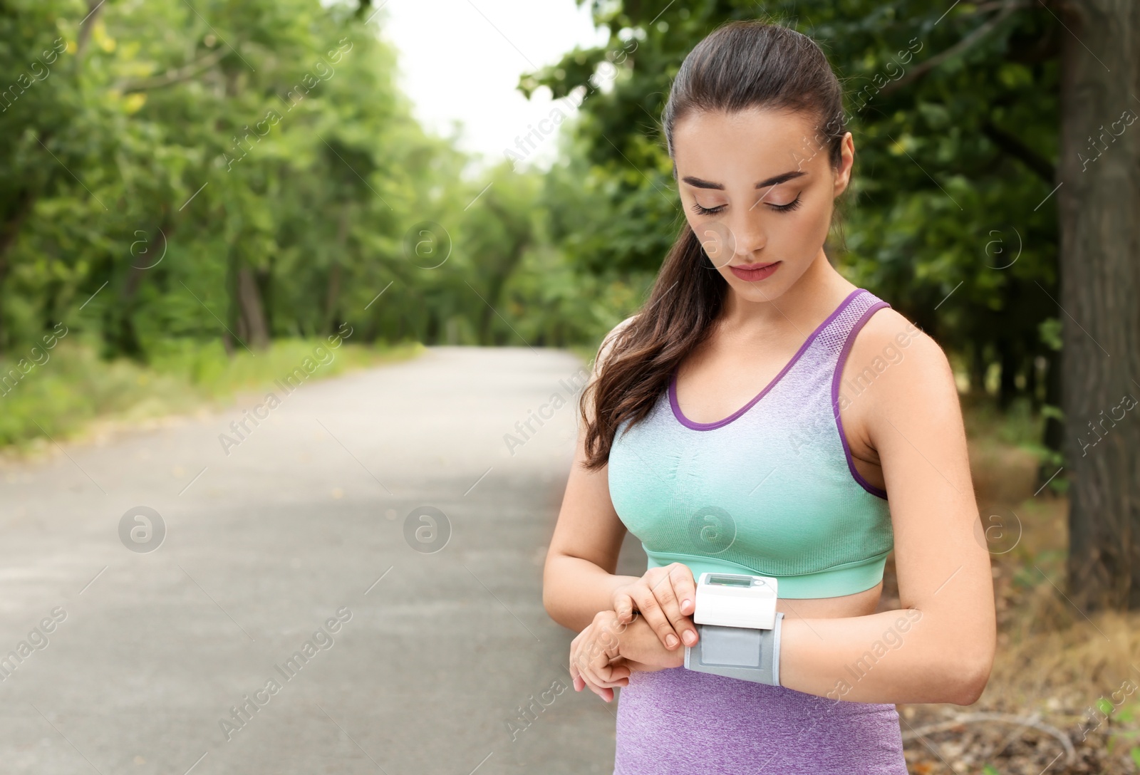 Photo of Young woman checking pulse with medical device after training in park. Space for text