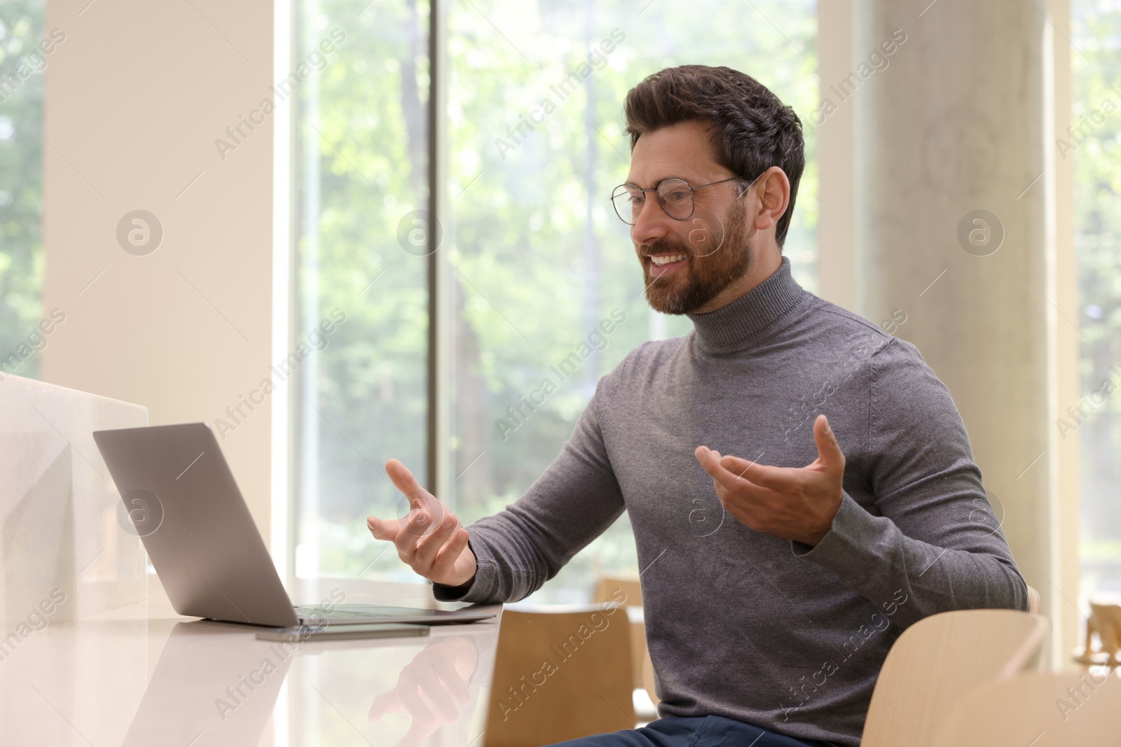 Photo of Man having video chat via laptop at table in cafe