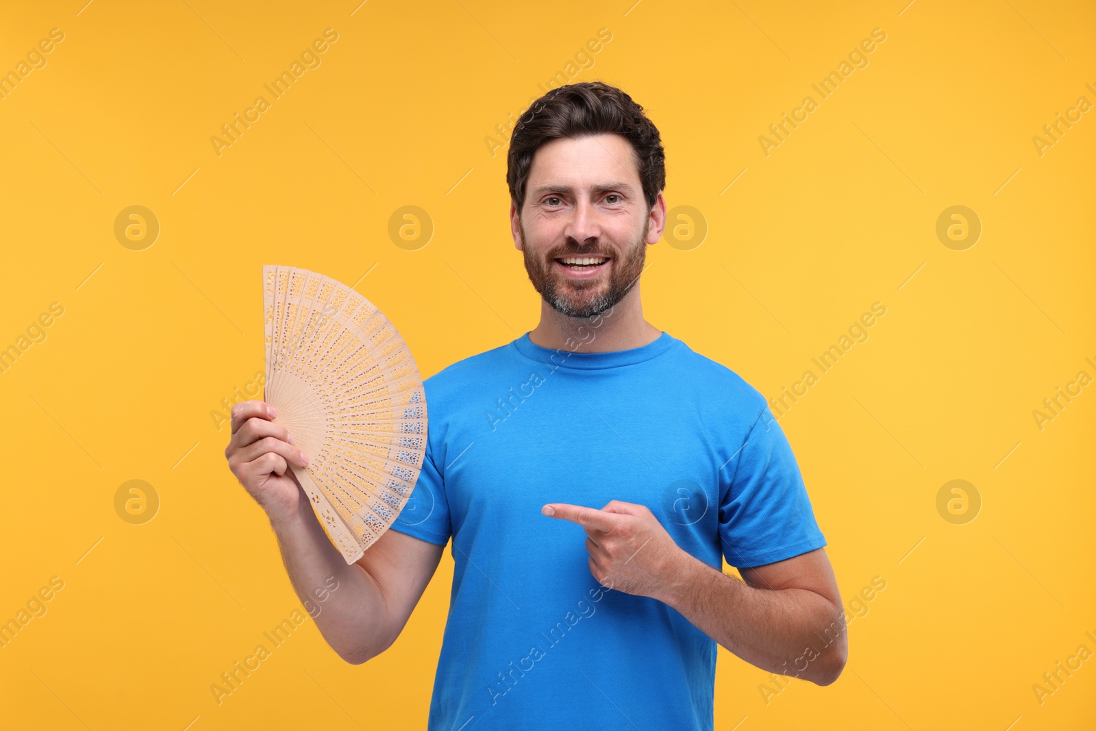 Photo of Happy man holding hand fan on orange background