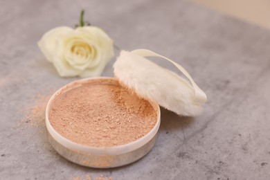 Face powder, puff applicator and rose flower on grey textured table, closeup