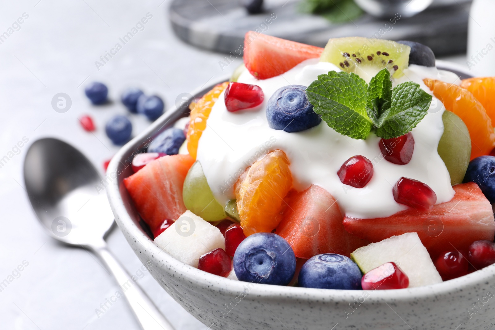 Photo of Delicious fruit salad with yogurt in bowl on table, closeup