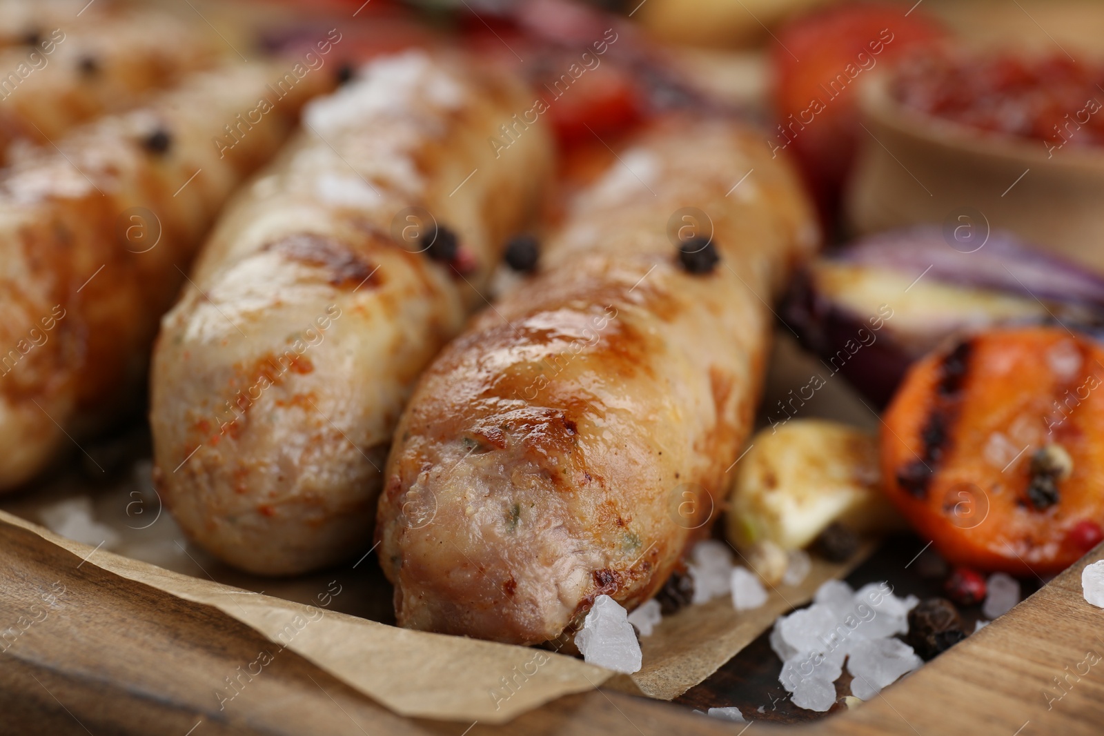 Photo of Tasty grilled sausages with vegetables on wooden board, closeup