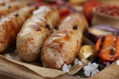 Photo of Tasty grilled sausages with vegetables on wooden board, closeup