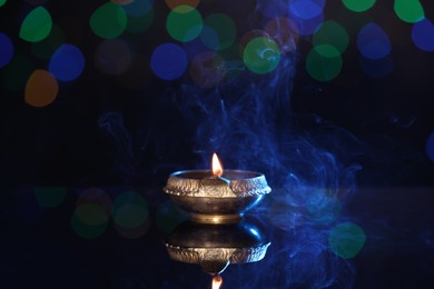 Lit diya on dark background with blurred lights, space for text. Diwali lamp