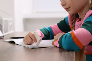 Girl erasing mistake in her homework at wooden table indoors, closeup