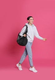 Beautiful woman with sports bag on pink background