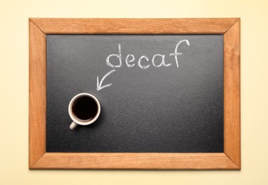 Photo of Chalkboard with word decaf and cup of coffee on beige background, top view