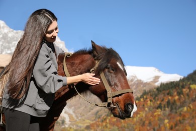 Photo of Young woman stroking horse in mountains on sunny day. Beautiful pet