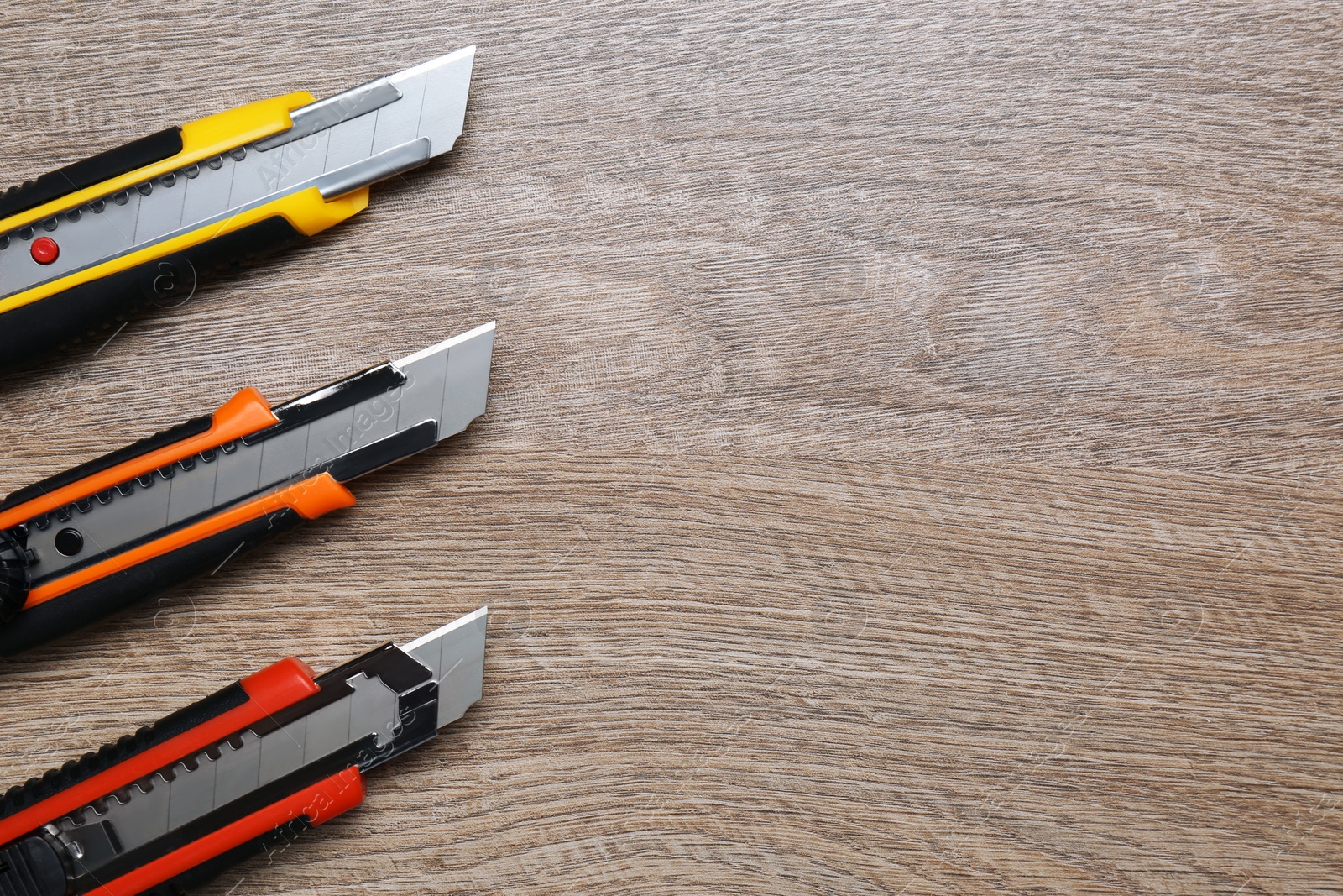 Photo of Three different utility knives on wooden table, flat lay. Space for text