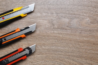 Three different utility knives on wooden table, flat lay. Space for text