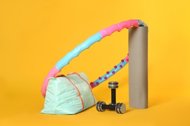 Hula hoop, yoga mat, gym bag and dumbbells on yellow background