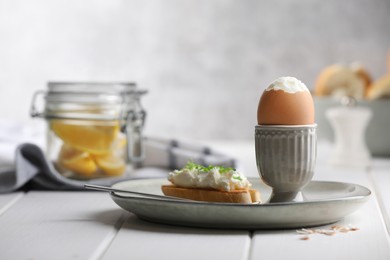 Fresh soft boiled egg in cup and sandwich on white wooden table. Space for text