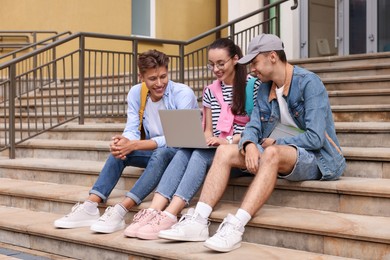 Photo of Happy young students studying together with laptop on steps outdoors