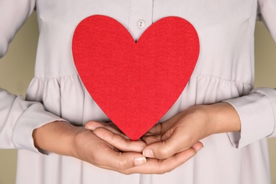 Photo of Young woman holding red heart on color background, closeup