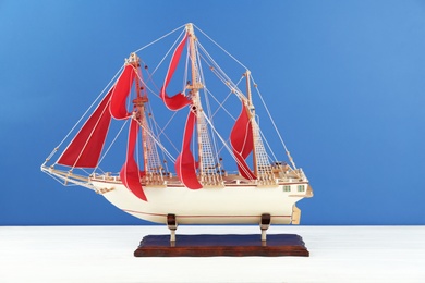Photo of Miniature model of old ship with red sails on white table against blue background