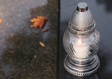 Grave lantern with burning candle on granite surface in cemetery, space for text