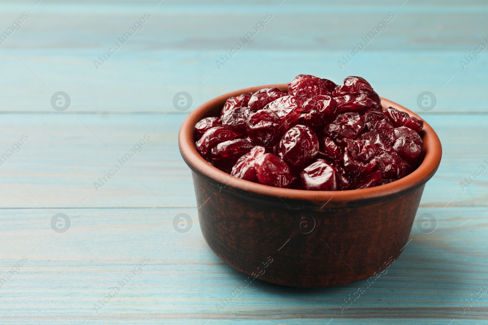 Photo of Tasty dried cranberries in bowl on light blue wooden table, closeup. Space for text