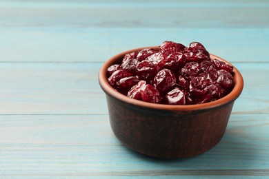 Photo of Tasty dried cranberries in bowl on light blue wooden table, closeup. Space for text