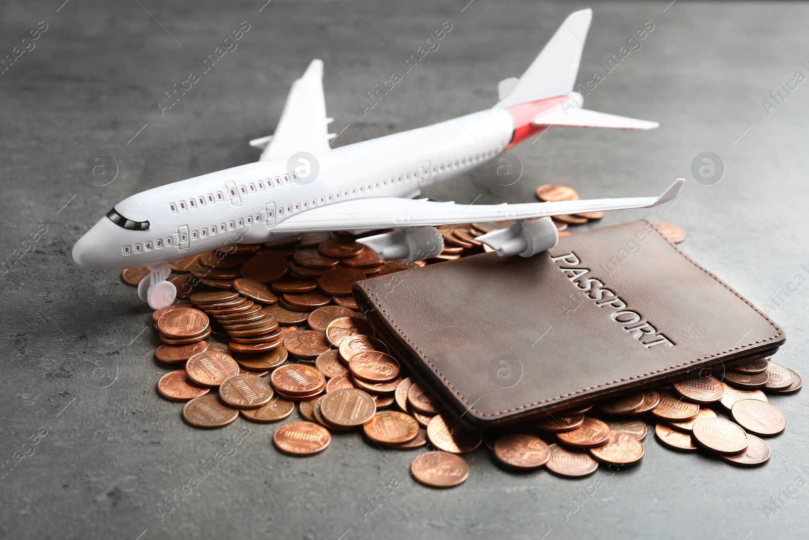 Photo of Pile of coins, passport and plane model on grey background