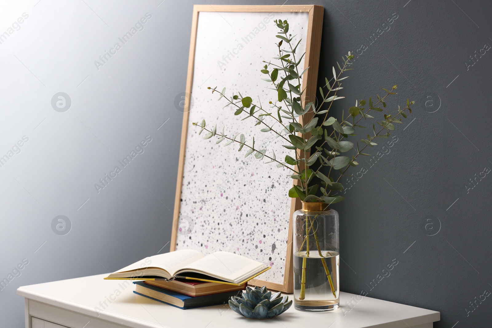 Photo of Beautiful eucalyptus branches on white table near black wall in modern room. Interior design