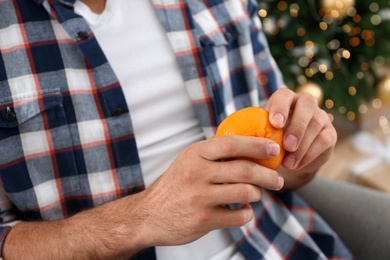 Man with tangerine near Christmas tree, closeup