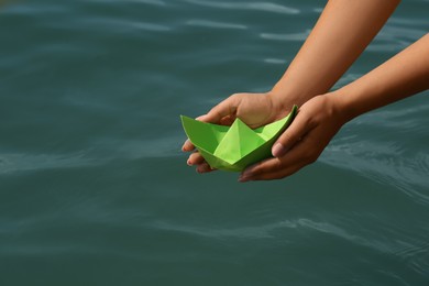 Photo of Woman holding light green paper boat near sea, closeup
