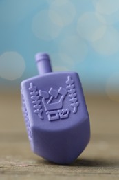 Photo of Hanukkah celebration. Dreidel with jewish letters on wooden table against light blue background with blurred lights, closeup