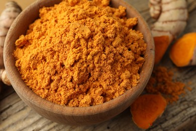 Photo of Aromatic turmeric powder and raw roots on wooden table, closeup