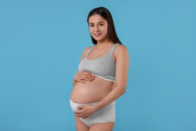 Beautiful pregnant woman in comfortable maternity underwear on light blue background