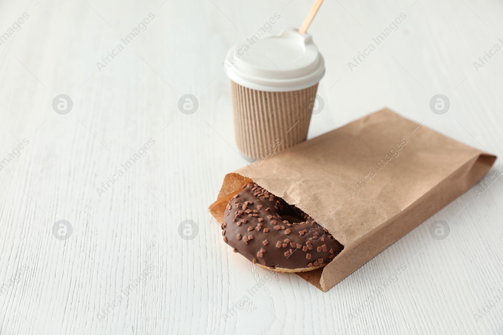 Photo of Tasty donut in paper bag and coffee on wooden table. Space for text