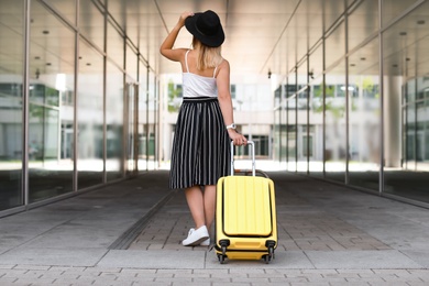 Young woman with yellow carry on suitcase outdoors